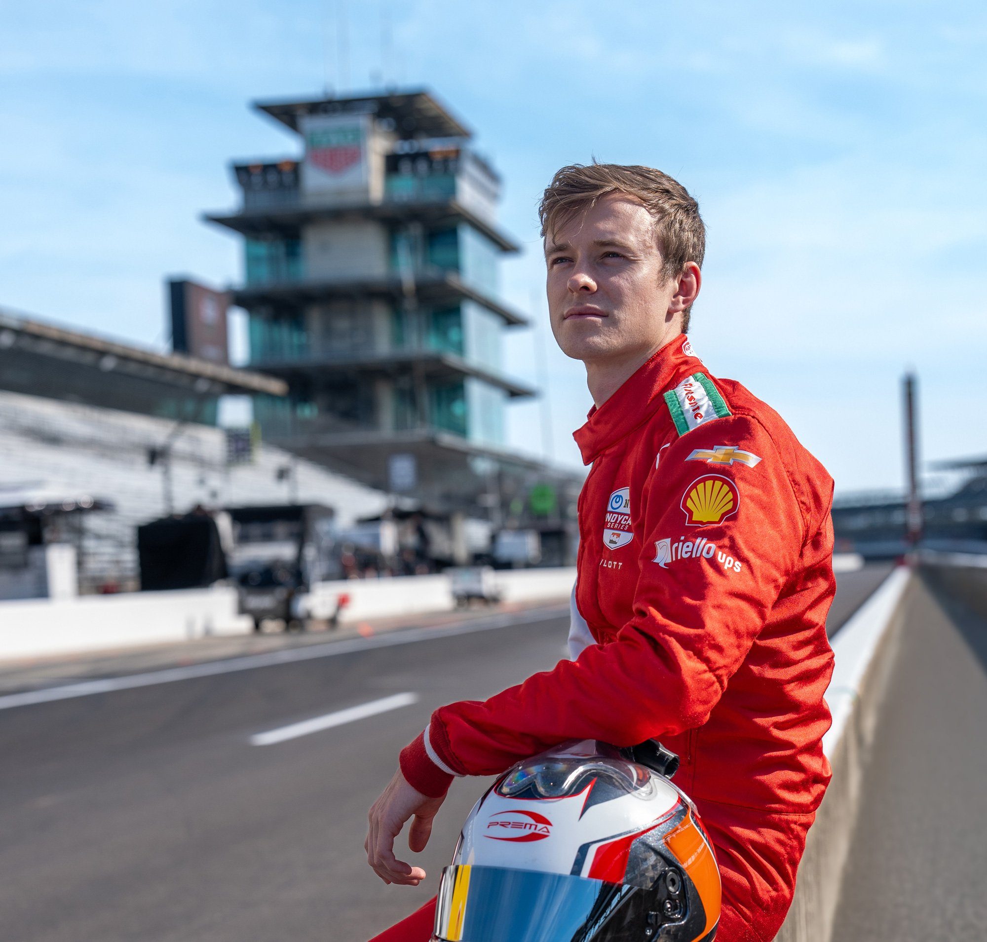A PREMA driver on the front straight at Indianapolis holding his helmet
