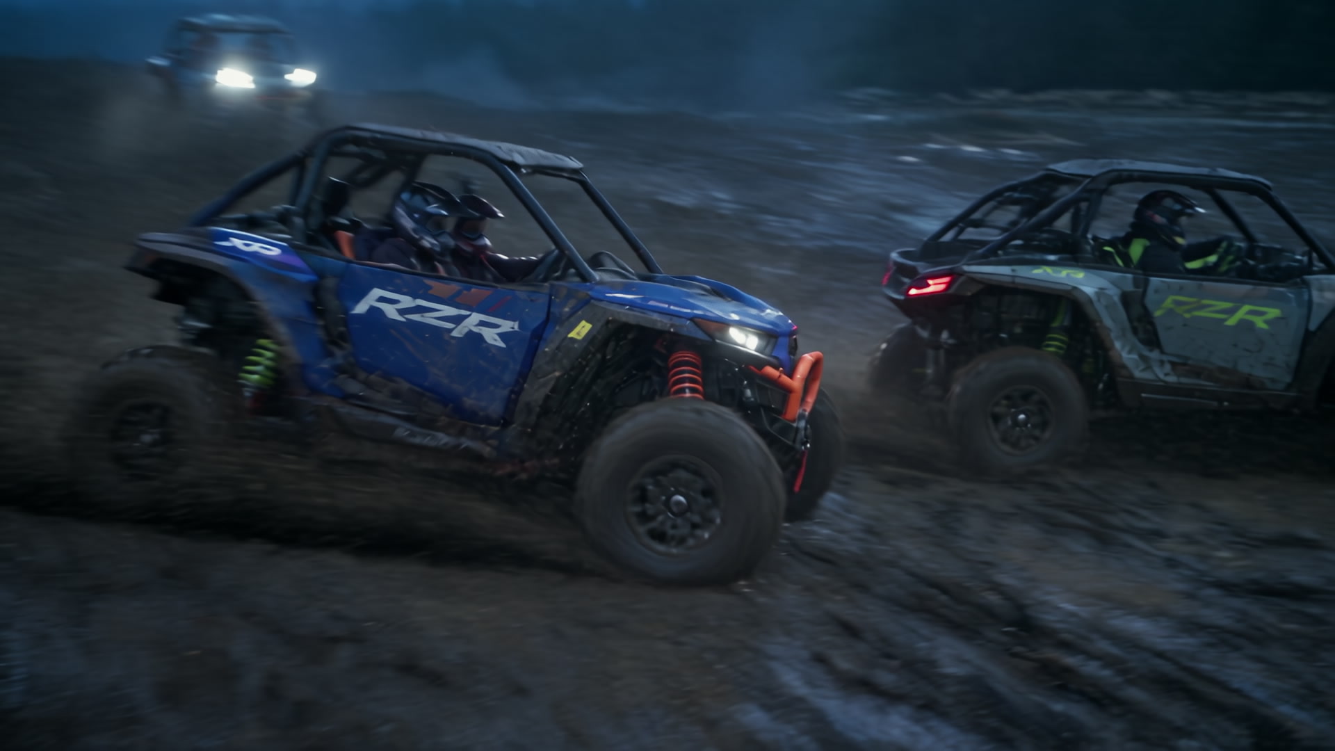 Blue and green Polaris RZRs racing across wet ground in Night Ride